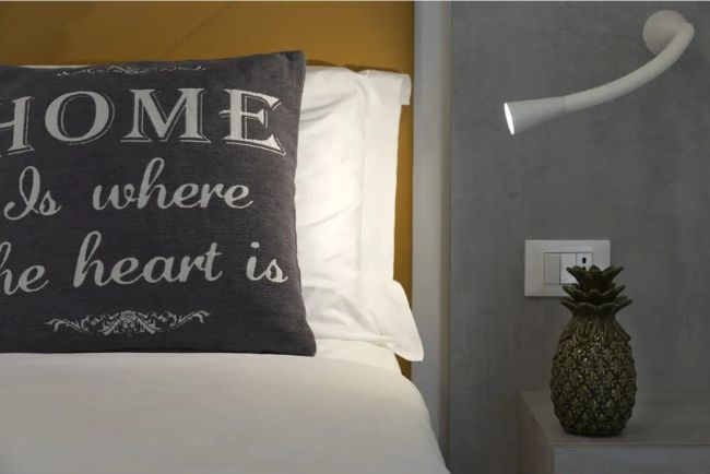 Hotel Caorle All'Orologio Dettaglio letto Camera Ananas Kiwi con cuscino scuro "Home is where the heart is", testiera gialla e soprammobile a forma di ananas sul comodino.