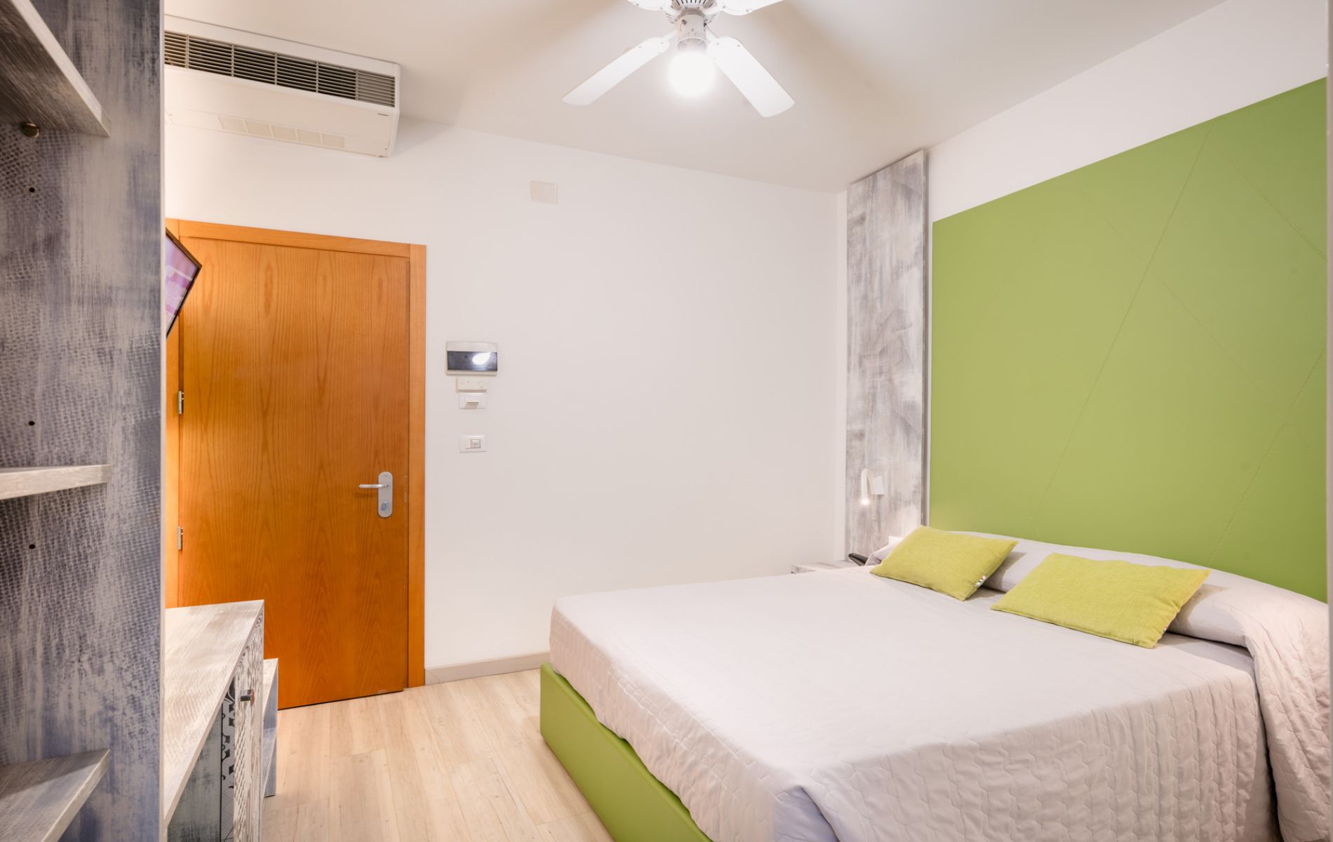 Vista della zona notte nella camera Ananas & Kiwi all'Hotel All'Orologio di Caorle: letto matrimoniale, arredi moderni e atmosfera luminosa.
