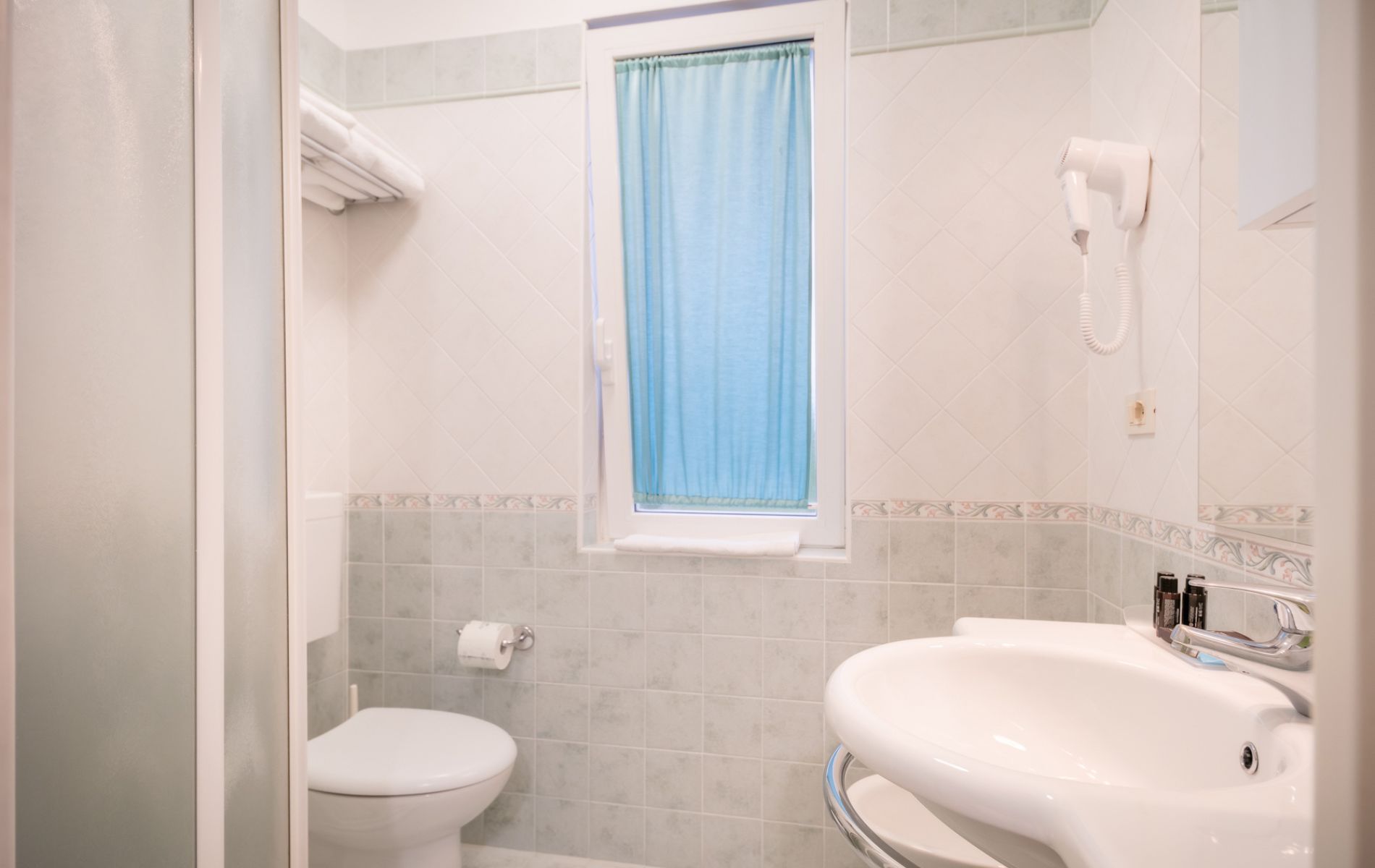 Bagno moderno dell'Hotel All'Orologio a Caorle: box doccia in cristallo, sanitari bianchi contemporanei e illuminazione luminosa.