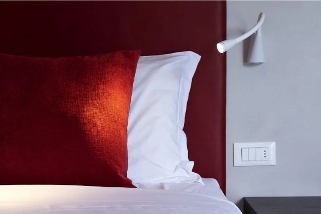 Hotel Caorle All'Orologio Primo piano testiera letto rosso intenso e cuscino arancione testurizzato della Camera Cherry Plus, con luce da lettura bianca accesa.