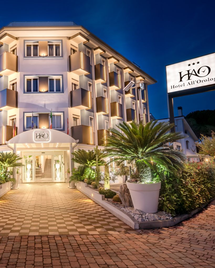 Facciata esterna notturna Hotel All'Orologio Caorle con luci soffuse e insegna illuminata.