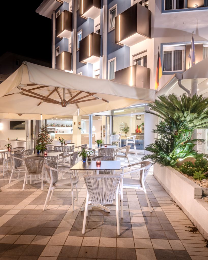 Terrazza esterna dell'Hotel All'Orologio a Caorle con area verde, tavolini e sedie per momenti di relax all'aperto.