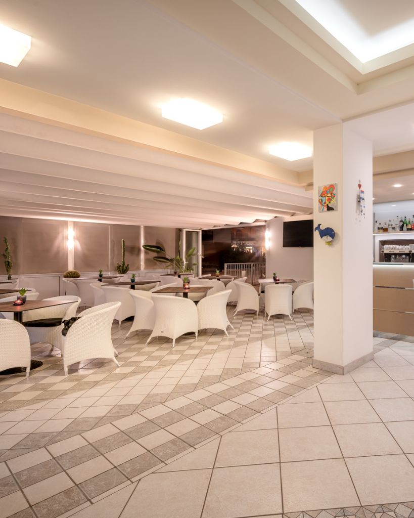Terrazza bar coperta dell'Hotel All'Orologio a Caorle, ambiente moderno e luminoso con tavolini per la colazione e il relax.