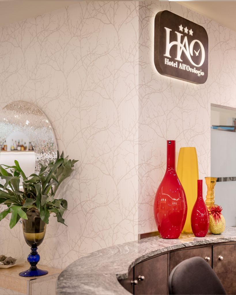 Dettaglio d'arredo alla reception dell'Hotel All'Orologio a Caorle: eleganti vasi in vetro di Murano colorato su un mobile di design.
