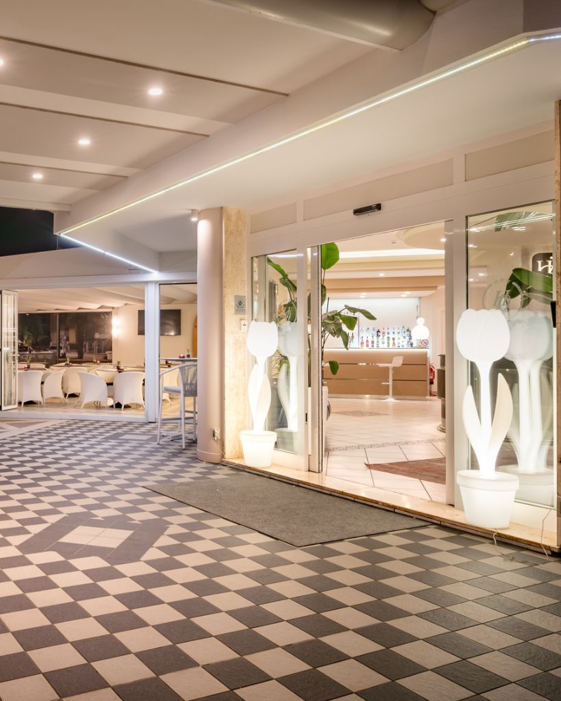 Ingresso principale dell'Hotel All'Orologio a Caorle con insegna luminosa e ampie vetrate moderne.