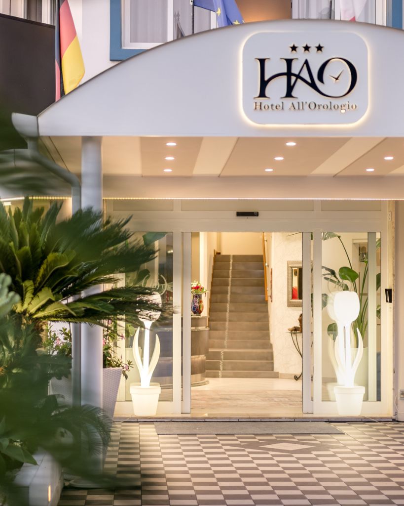 Facciata e ingresso frontale dell'Hotel All'Orologio a Caorle con insegna principale e design moderno.