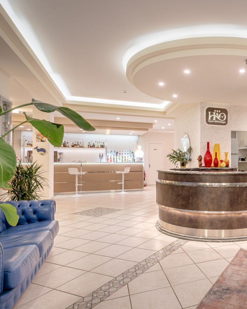 Hall moderna dell'Hotel All'Orologio a Caorle con piante di palme decorative e arredamento elegante.