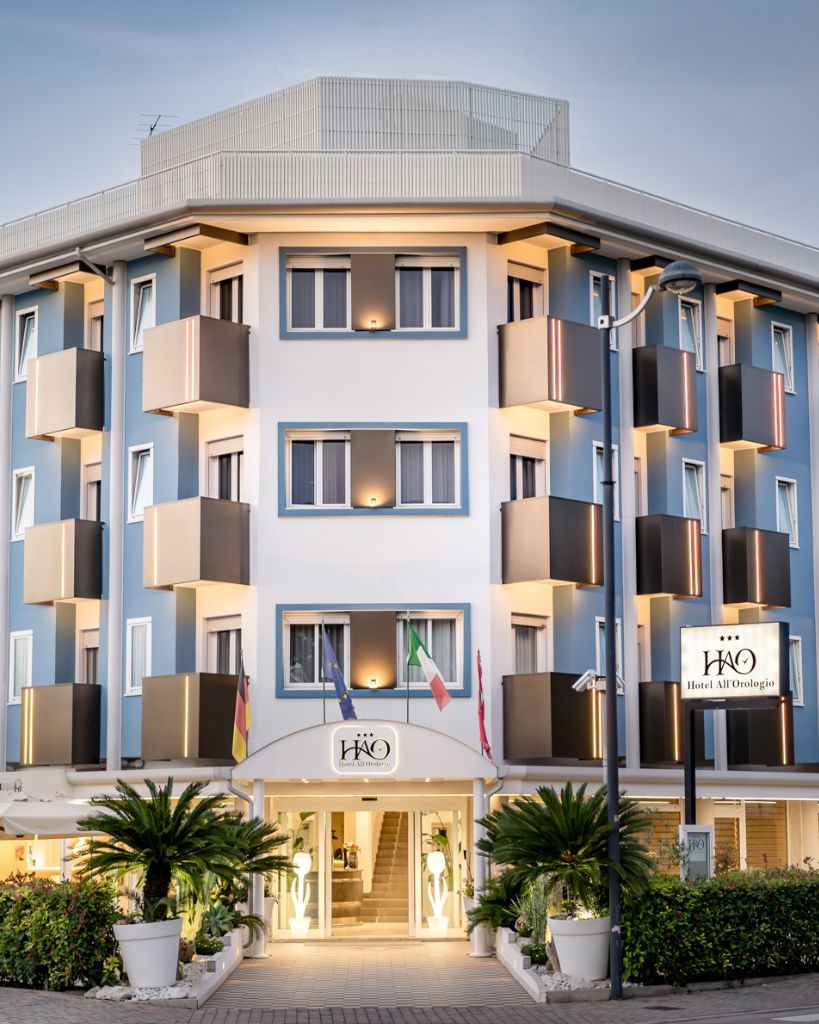 Facciata moderna dell'Hotel All'Orologio a Caorle illuminata dalla luce calda del tramonto.
