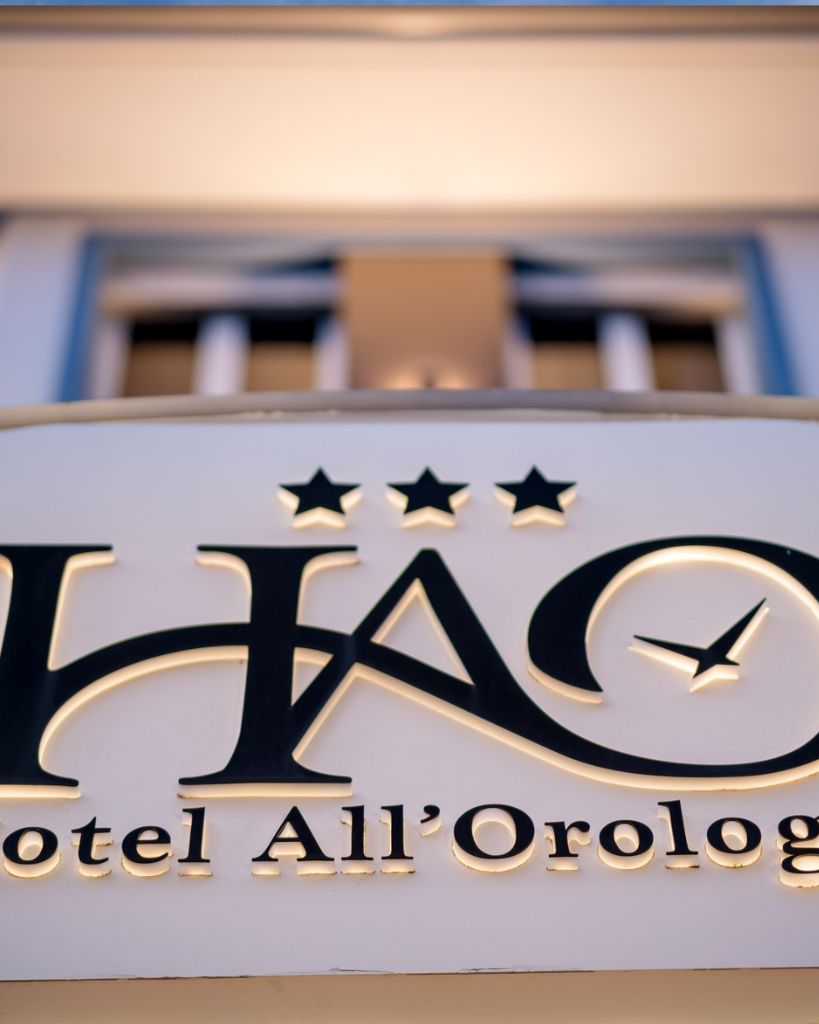 Dettaglio dell'insegna dell'Hotel All'Orologio a Caorle con logo a forma di orologio e lettering moderno.