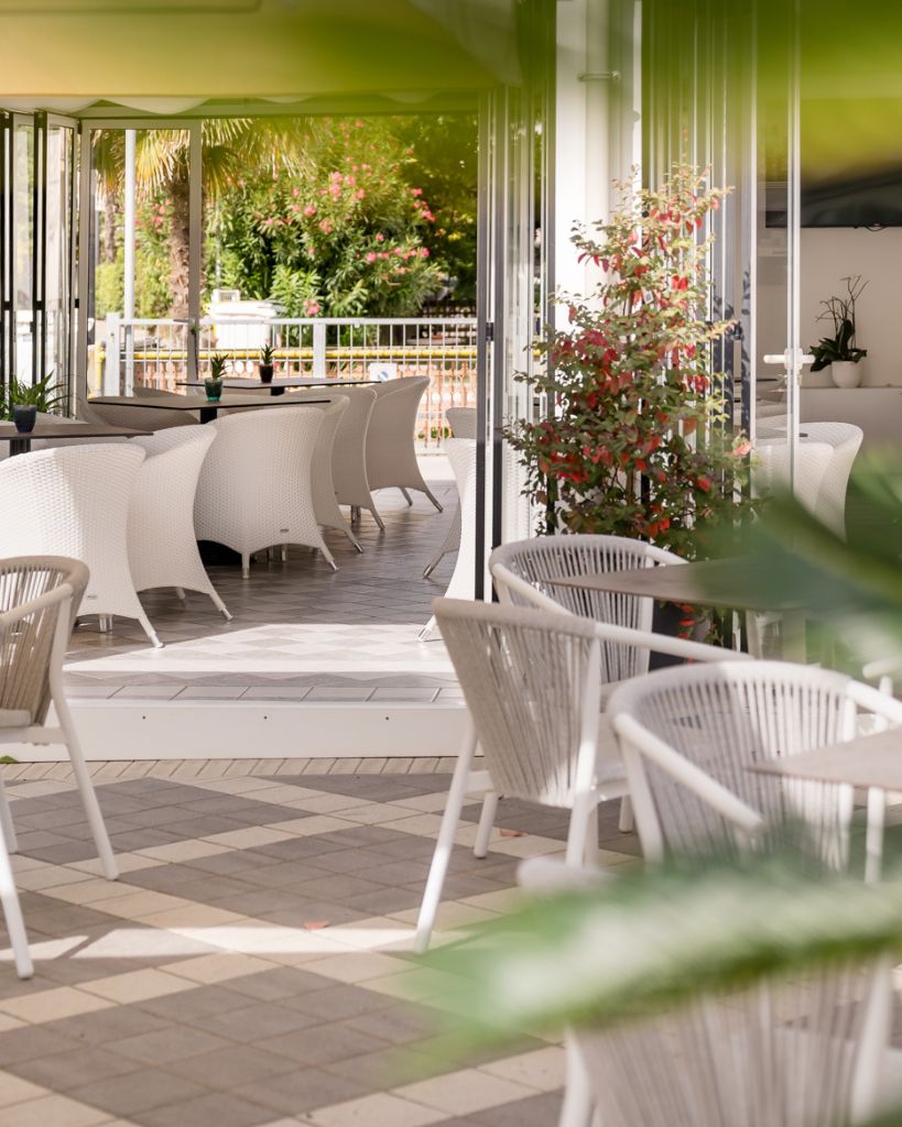Giardino esterno dell'Hotel All'Orologio a Caorle con piante rigogliose, siepi curate e pavimentazione moderna.