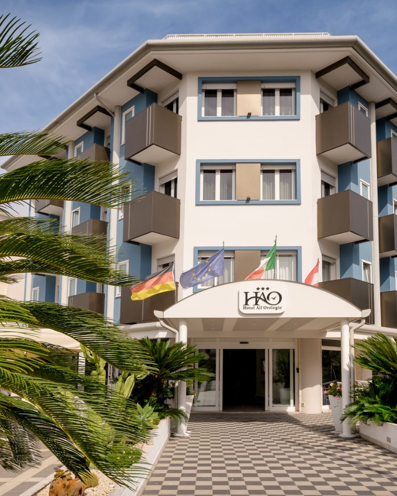 Bandiere istituzionali che sventolano all'ingresso dell'Hotel All'Orologio a Caorle, simbolo di accoglienza e ospitalità internazionale.