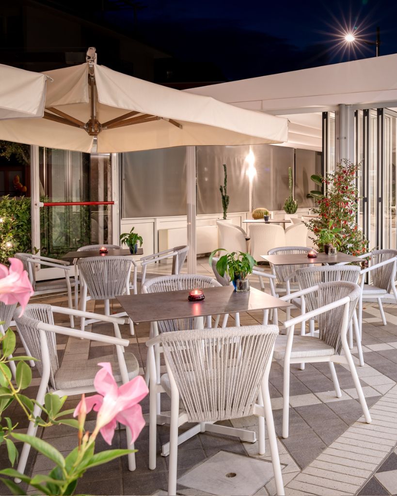 Terrazza esterna del bar dell'Hotel All'Orologio a Caorle di sera, con illuminazione soffusa, tavolini e poltrone di design moderno.