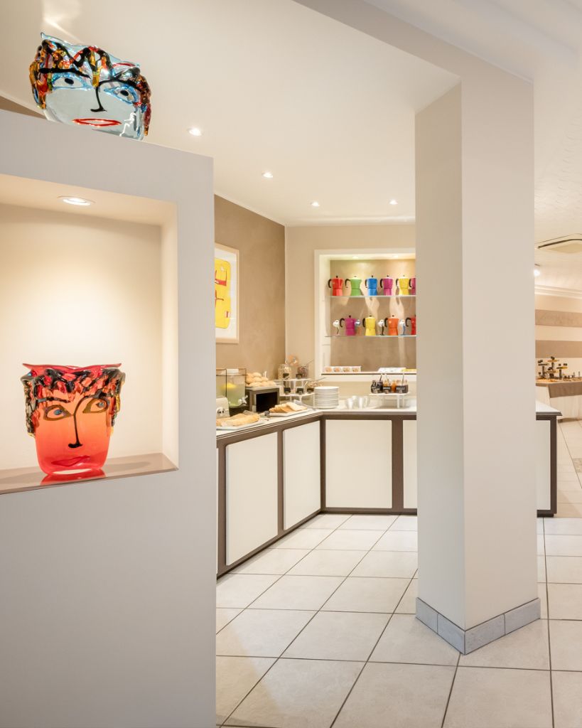 Sala colazione luminosa dell'Hotel All'Orologio a Caorle con tavoli moderni, sedie bianche e ampie vetrate.