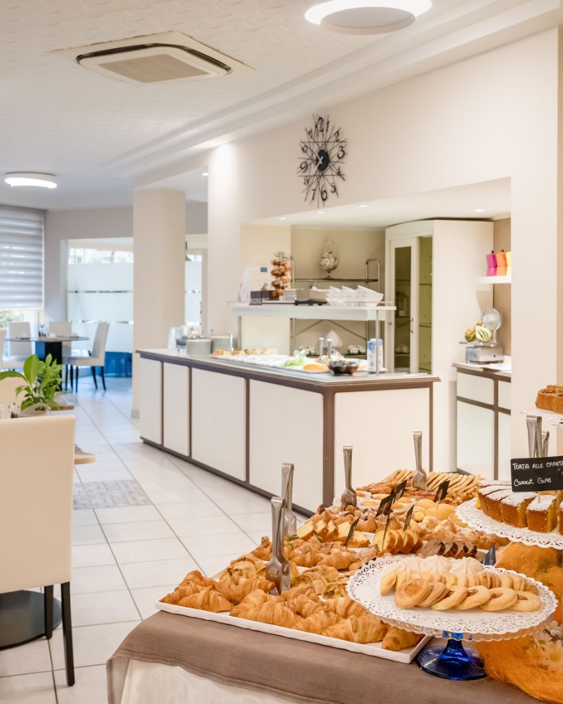 Angolo buffet della colazione presso l'Hotel All'Orologio a Caorle, con selezione di prodotti freschi, dolci e salati in un ambiente moderno.