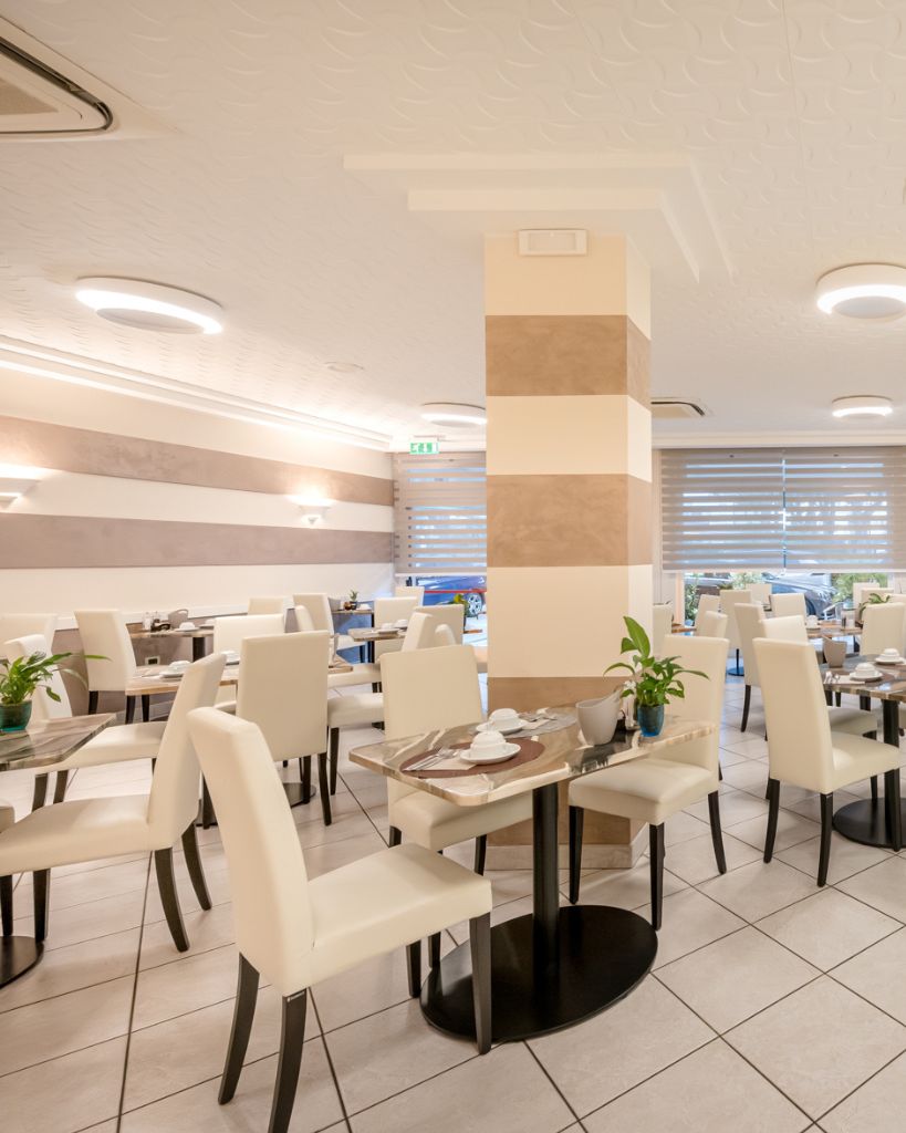 Tavolo apparecchiato per la colazione all'Hotel All'Orologio di Caorle, dettaglio degli arredi moderni e dell'ambiente luminoso della sala.