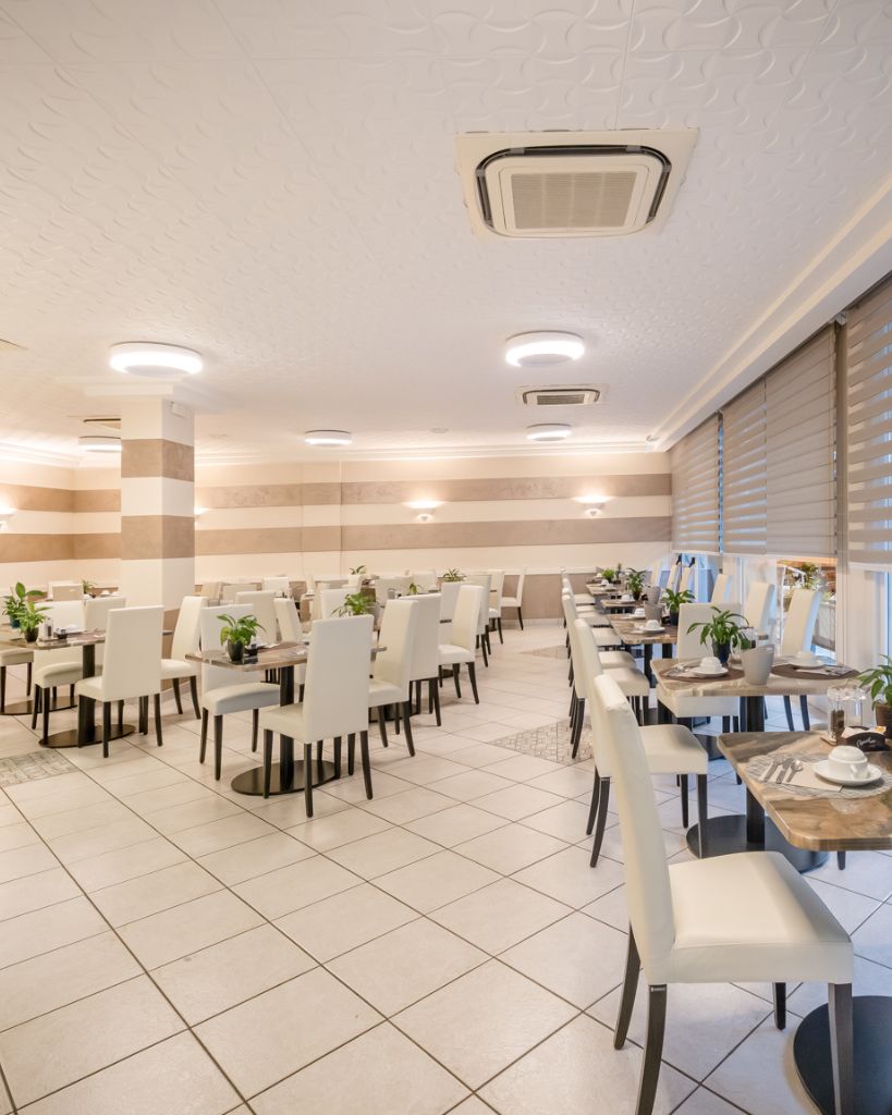 Allestimento dei tavolini nella moderna sala colazione dell'Hotel All'Orologio a Caorle, ambiente luminoso e ordinato.