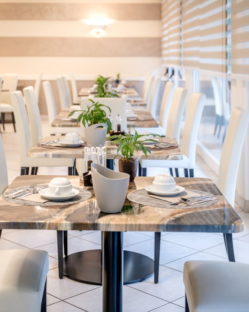 Tavolini e sedie moderne nella zona colazione e bar dell'Hotel All'Orologio a Caorle, ambiente dal design contemporaneo e luminoso.