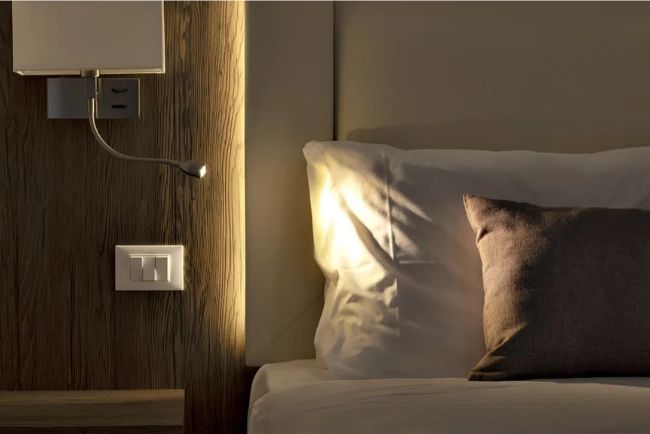 Hotel Caorle All'Orologio Dettaglio del letto e della lampada da lettura nella Camera Harmony con finiture in legno naturale.