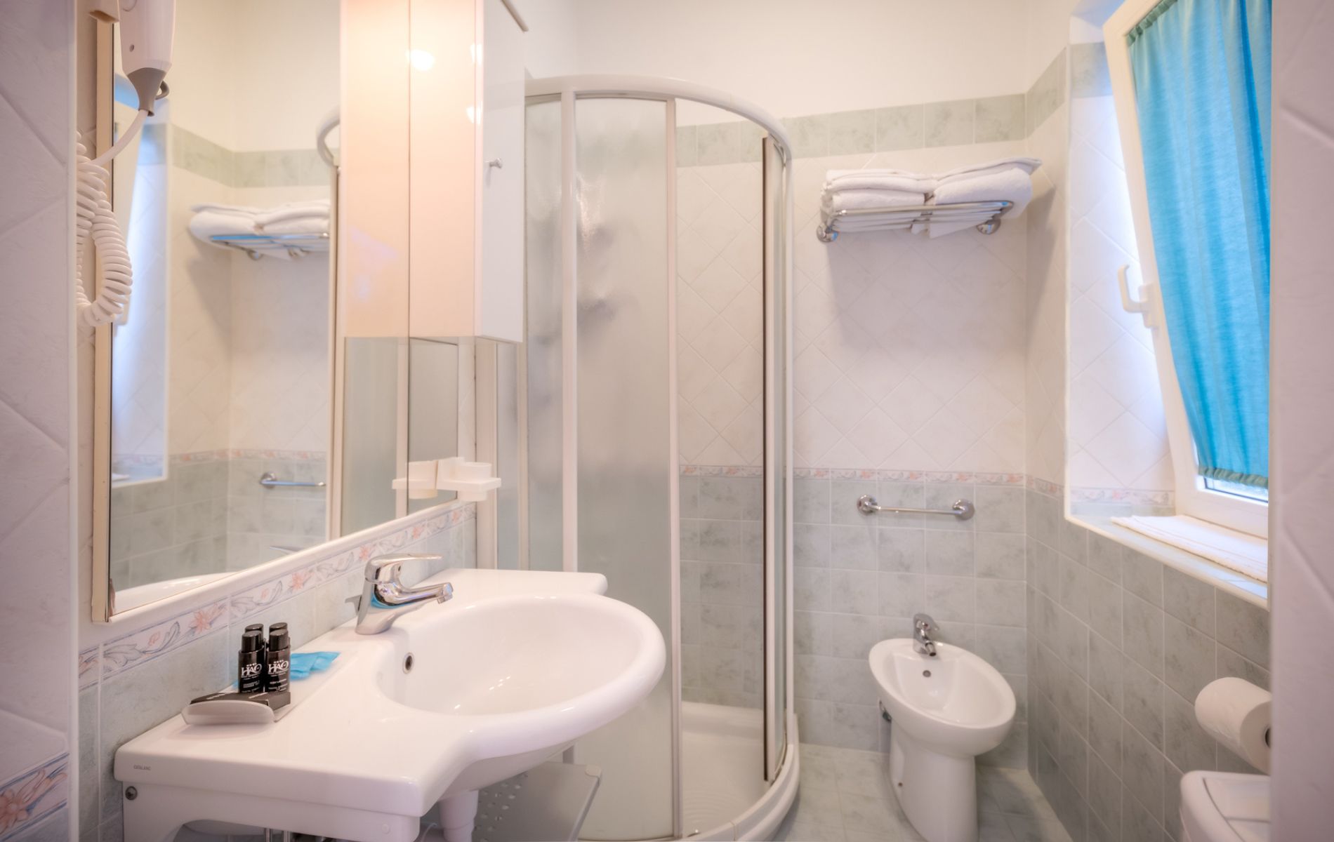 Bagno della camera Tropical presso l'Hotel All'Orologio a Caorle: ambiente moderno con box doccia, sanitari sospesi e kit di cortesia.